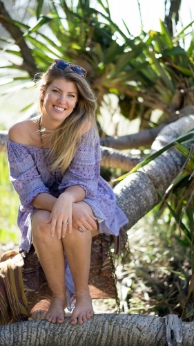 Girl sitting on tree branch on beach - Australian Stock Image