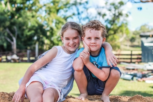 Girl with arm around boy sitting on mound of dirt - Australian Stock Image