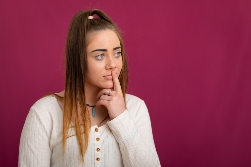 girl with one finger to lips against dark pink background - Australian Stock Image