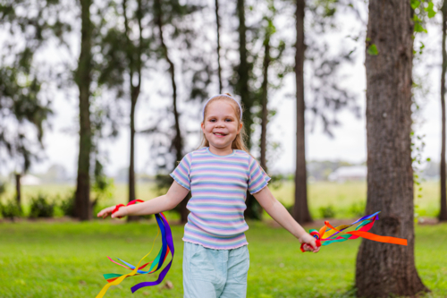 Girl with rainbow streamers running around outside in country - Australian Stock Image