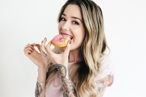 Girl with visible tattoos eating a pink donut - Australian Stock Image