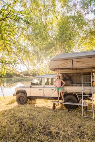 Girls beside four wheel drive with roof top tent by a river in afternoon light