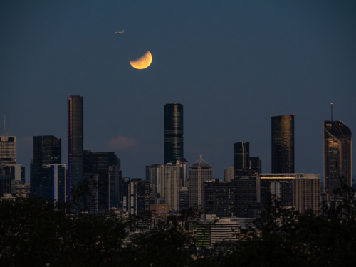 Glowing eclipse of the full moon shining over city skyline - Australian Stock Image