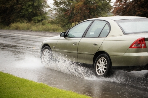 gold car driving through a puddle on a rainy day creating a splash - Australian Stock Image