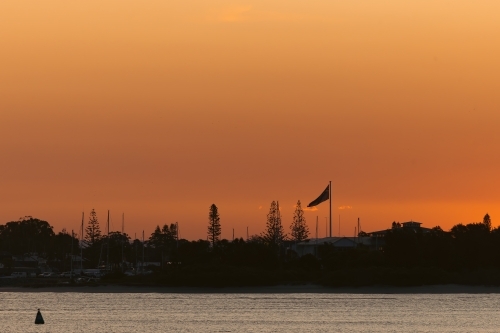 Golden hour view across the bay at Port Macquarie with silhouette of Australian flag - Australian Stock Image