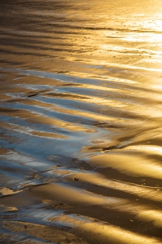 Golden light reflecting off a rippled wet beach - Australian Stock Image