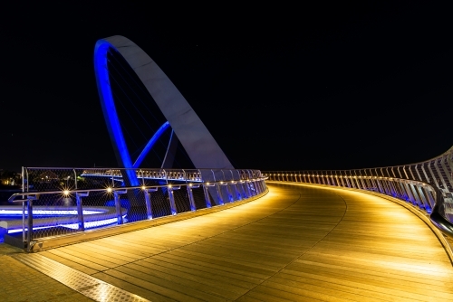 Golden lit path curving onto arched bridge with blue lighting and night sky - Australian Stock Image