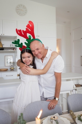 Grandfather and granddaughter hugging at Christmas dining table - Australian Stock Image