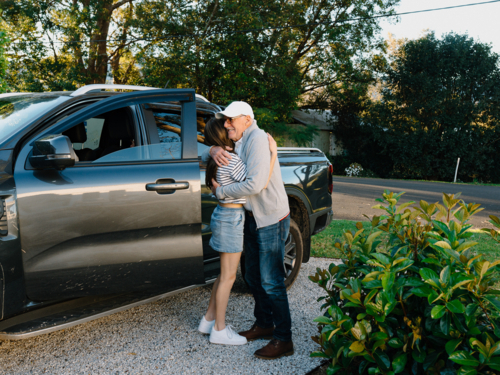 Grandfather embracing granddaughter outside by the car - Australian Stock Image