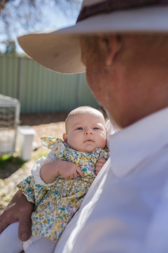 Grandfather looking down at granddaughter in arms - Australian Stock Image