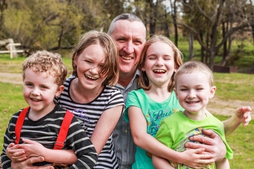 Grandfather sitting with grandchildren laughing - Australian Stock Image