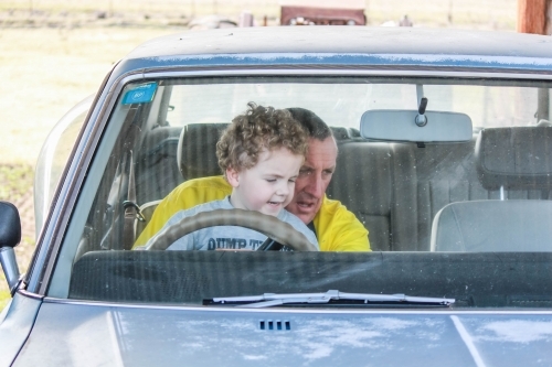 Grandfather sitting with grandson in old car - Australian Stock Image