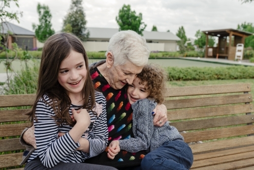 Grandmother hugging her grandchildren on a park bench at a retirement home - Australian Stock Image