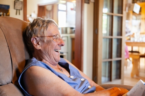 Grandmother sitting in chair inside laughing - Australian Stock Image