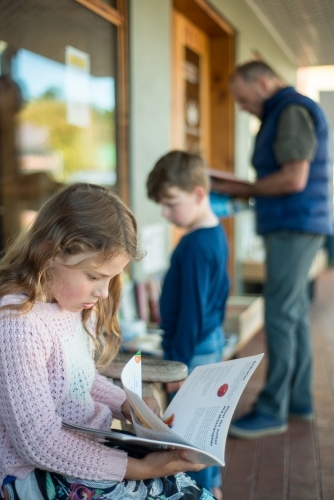 Grandpa with children looking at books at shop - Australian Stock Image