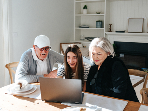 Grandparents sitting with their granddaughter in front of a laptop on the table. - Australian Stock Image