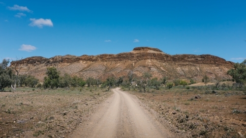 Gravel road leading towards imposing rock formation in the outback - Australian Stock Image