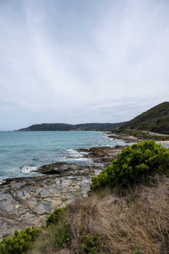 Great Ocean Road scenery with ocean coming to rocky shore under overcast sky - Australian Stock Image