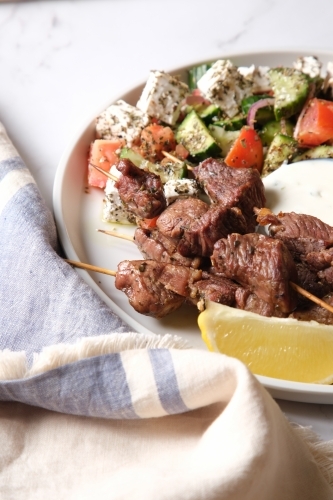 Grilled meat served on a white plate with fries, white sauce, vegetable salad, and pita bread - Australian Stock Image