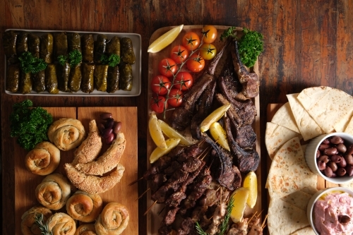 Grilled meats and bread rolls with pita breads, side dishes, and stuffed vegetables on the side - Australian Stock Image