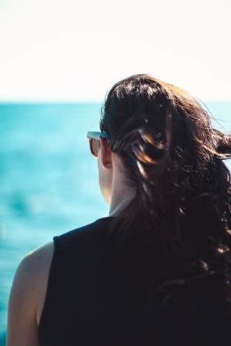 Hair blows behind woman as she stares out at the ocean - Australian Stock Image