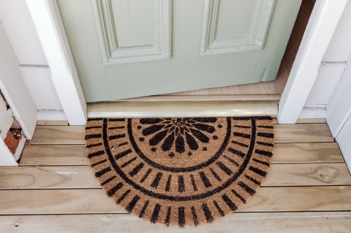 Half-circle coir doormat placed on a wooden floor in front of the door. - Australian Stock Image