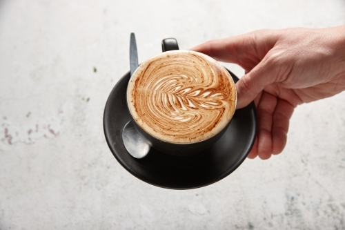 hand holding a saucer with a cup of coffee - Australian Stock Image