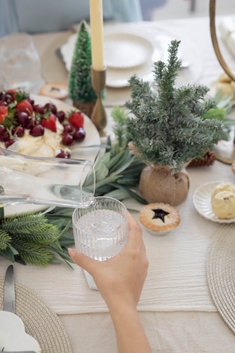 Hand holding glass of water at Christmas-decorated table - Australian Stock Image