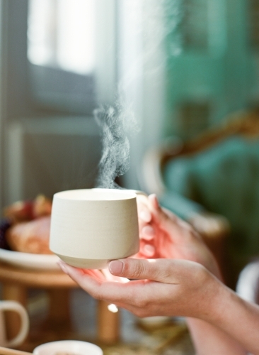 Delicate Hands holding a warm cup of tea with steam - Australian Stock Image