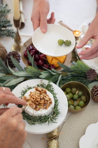 Hands slicing camembert at Christmas-decorated table - Australian Stock Image