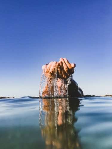 Hands together coming out of ocean with water flowing and reflection clear on clear sunny day - Australian Stock Image