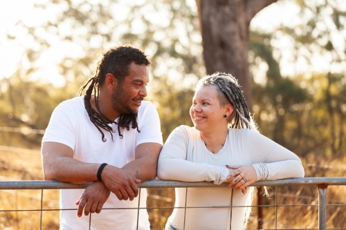 Happy aboriginal Australian couple leaning on farm gate together in country - Australian Stock Image