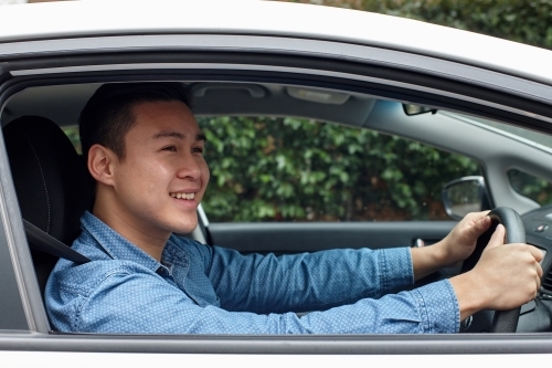 Happy Asian man driving in car looking out window - Australian Stock Image