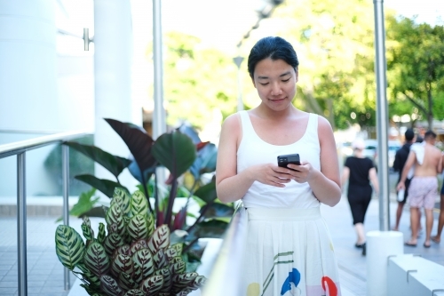 Happy Asian woman holding her mobile device - Australian Stock Image