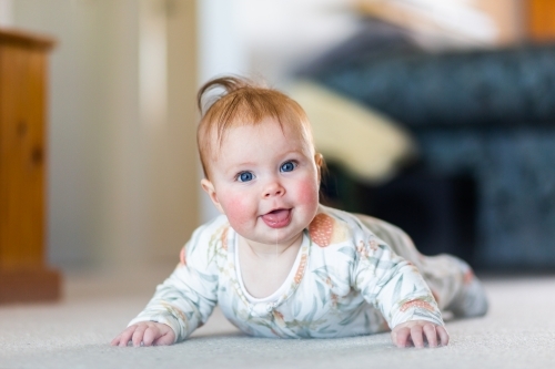 Happy baby girl learning to crawl doing tummy time on living room floor - Australian Stock Image