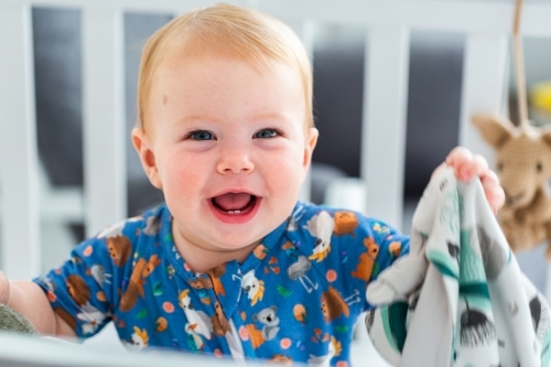 Happy baby in white cot with blanky toy - Australian Stock Image