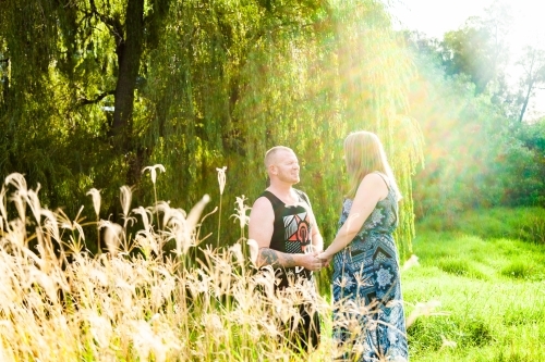 Happy backlit couple standing together in long grass - Australian Stock Image