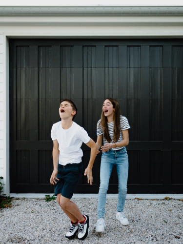 Happy brother and teen sister being silly together outside carport at home - Australian Stock Image