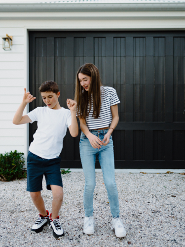Happy brother and teen sister being silly together outside carport at home - Australian Stock Image