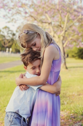 Happy brother hugs big sister in the park - Australian Stock Image