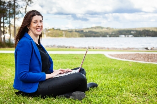 Happy business woman smiling at camera with laptop in park - Australian Stock Image