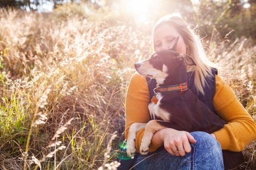 Happy country woman in her twenties with pet Australian Kelpie puppy dog in grass on farm - Australian Stock Image