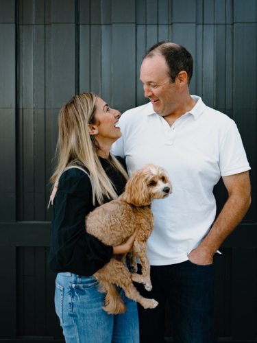 Happy couple looking at each other lovingly holding pet dog - Australian Stock Image