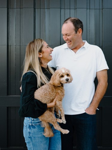 Happy couple looking at each other lovingly holding pet dog - Australian Stock Image