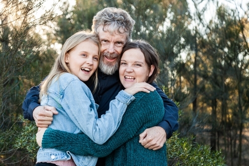 Happy dad with his two teenage daughters hug together outside - Australian Stock Image