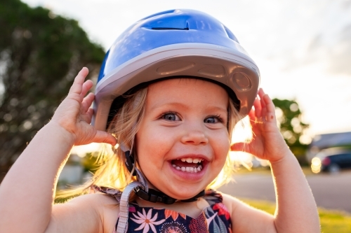 Happy delighted toddler girl wearing bike helmet for riding outside - Australian Stock Image