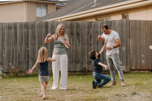 Happy family blowing and playing with bubbles in their yard. - Australian Stock Image