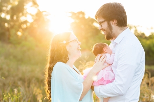 Happy family of three - parents with newborn outside in sunlight - Australian Stock Image