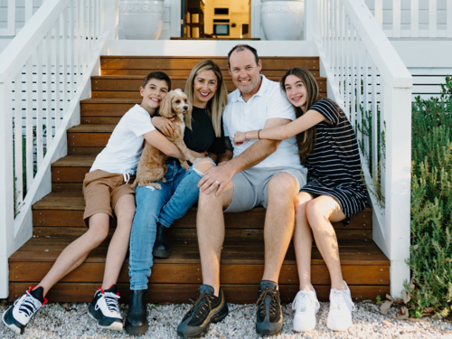 Happy family sitting on the steps of their home. - Australian Stock Image