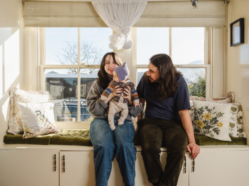 Happy family sitting together near windows inside brightly lit home - Australian Stock Image